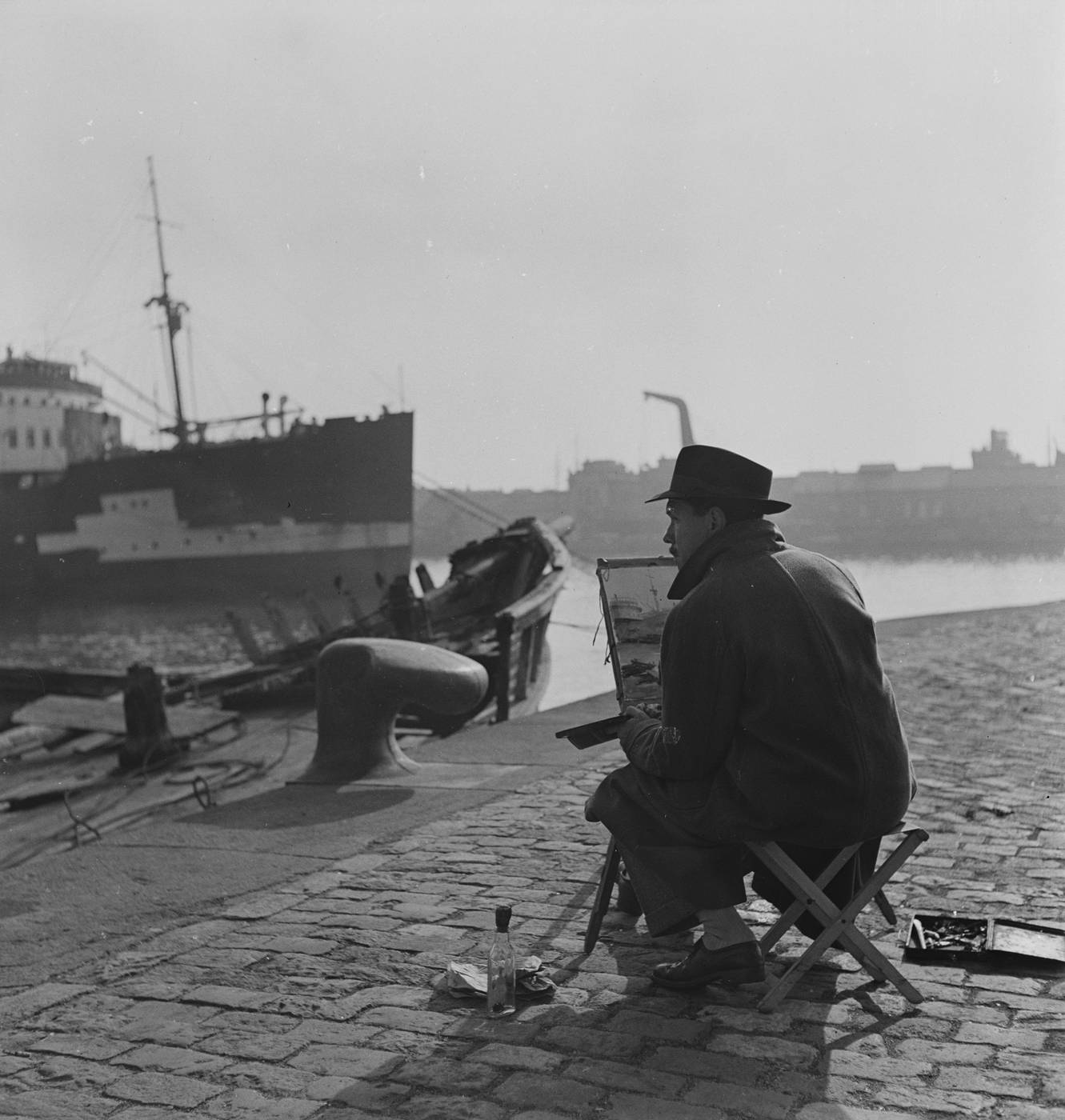Pintor trabajando al aire libre en el muelle del puerto de Barcelona, con buque amarrado al fondo. Fotografía de Joaquín Tusquets de Cabirol, c. 1950.