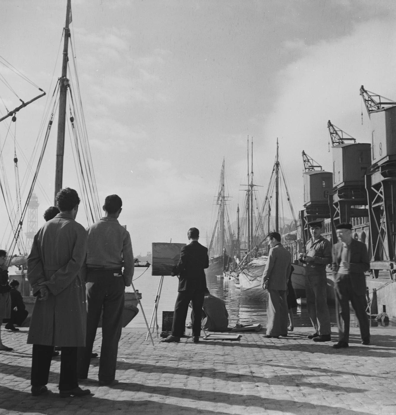 Pintor con caballete y observadores en el muelle del puerto de Barcelona, junto a grúas portuarias y veleros amarrados. Joaquín Tusquets de Cabirol, c. 1950.