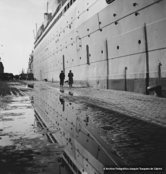 Transatlántico amarrado en el puerto de Barcelona con reflejos en el empedrado tras la lluvia. Joaquín Tusquets de Cabirol, c. 1950.